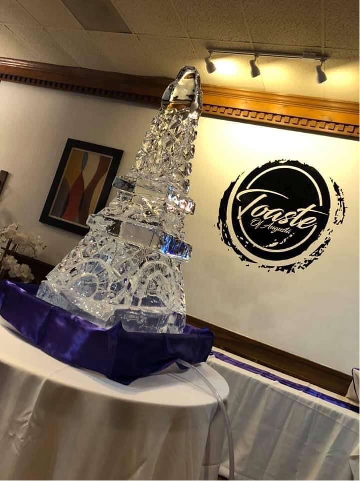 An ice sculpture of a tower sits on a table with a purple cloth. 