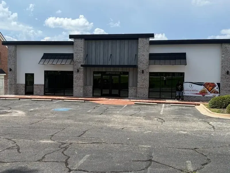 Exterior of a vacant commercial building with large windows and brick accents; overcast sky overhead.