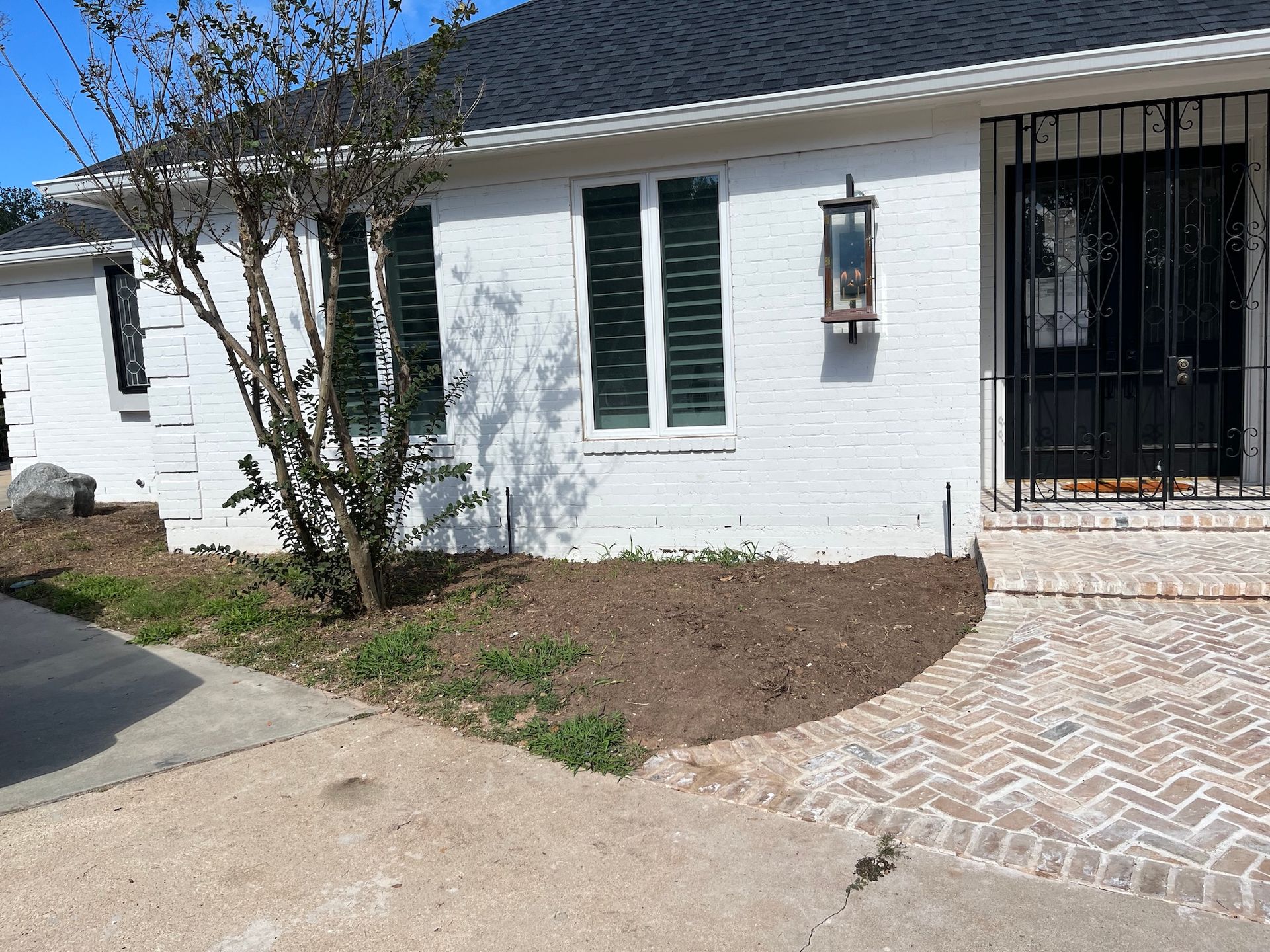 White-painted brick house with black shutters and door, small tree, and a brick pathway.