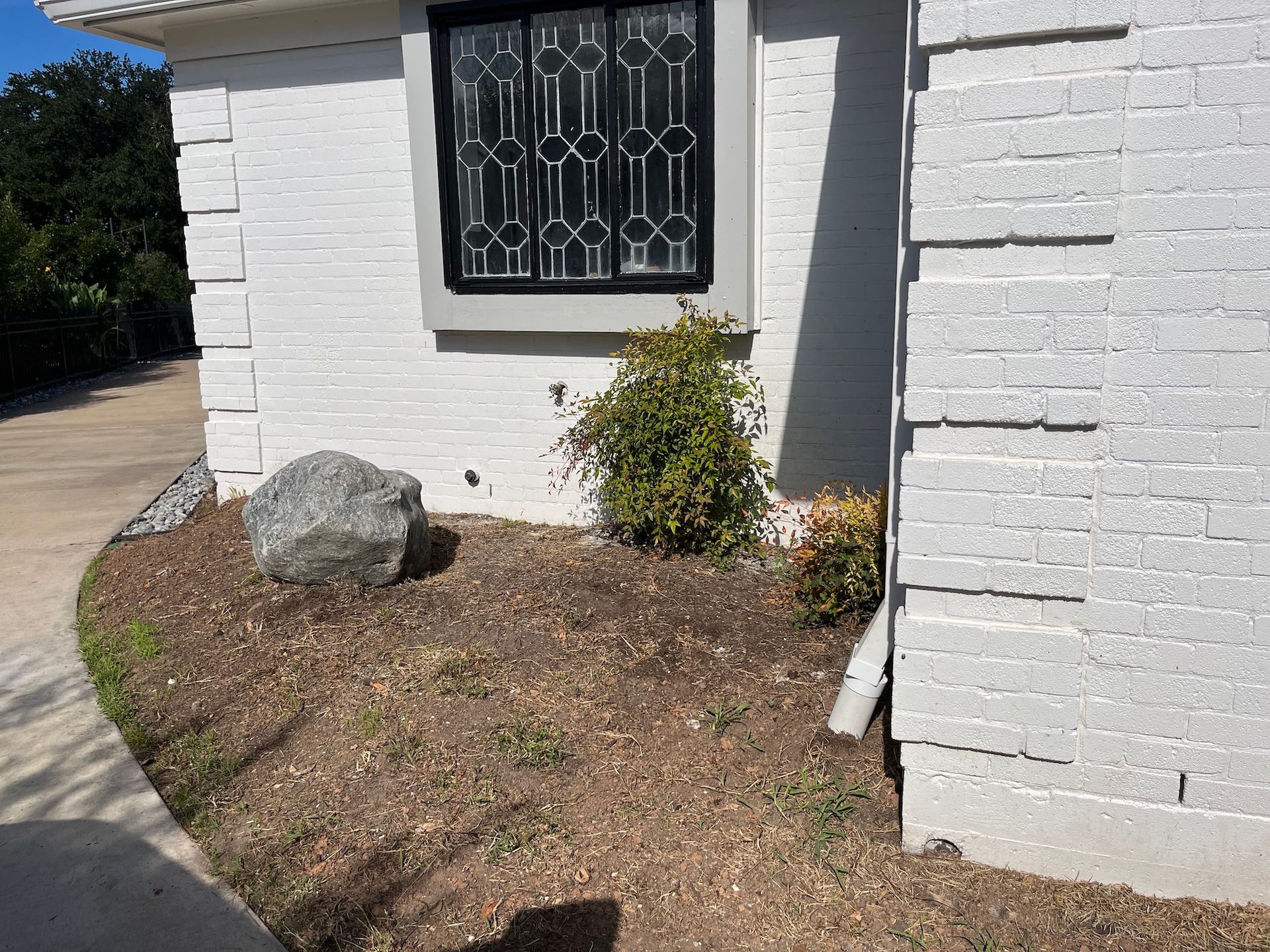 Exterior view of a house with a small rock garden in front, a window with decorative bars, and white textured siding.
