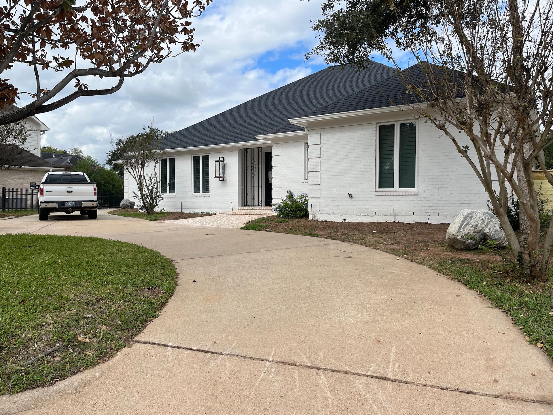 White brick house with black roof, driveway, and a pickup truck.