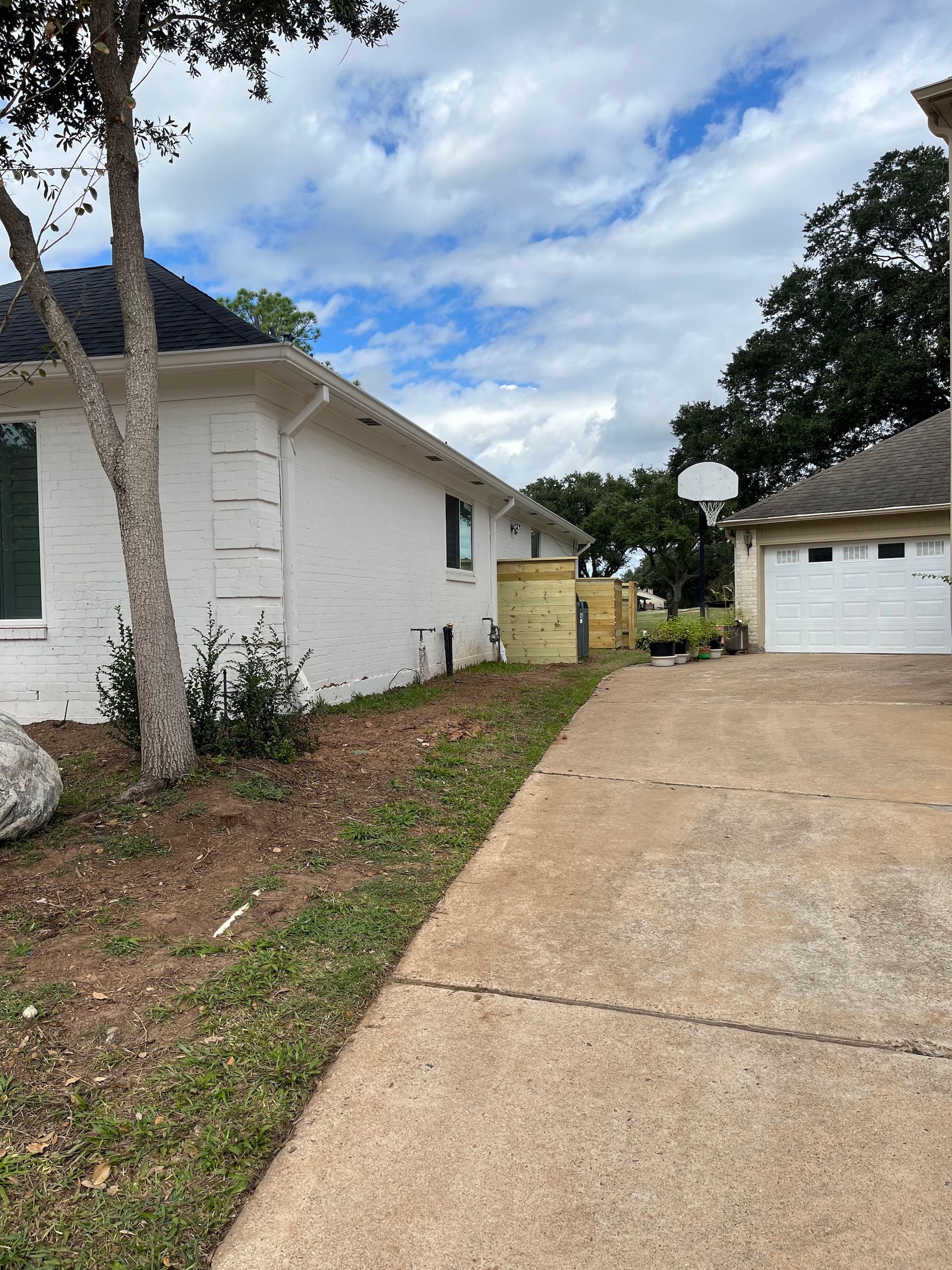 Side view of a white brick house, driveway, and garage under a cloudy sky.