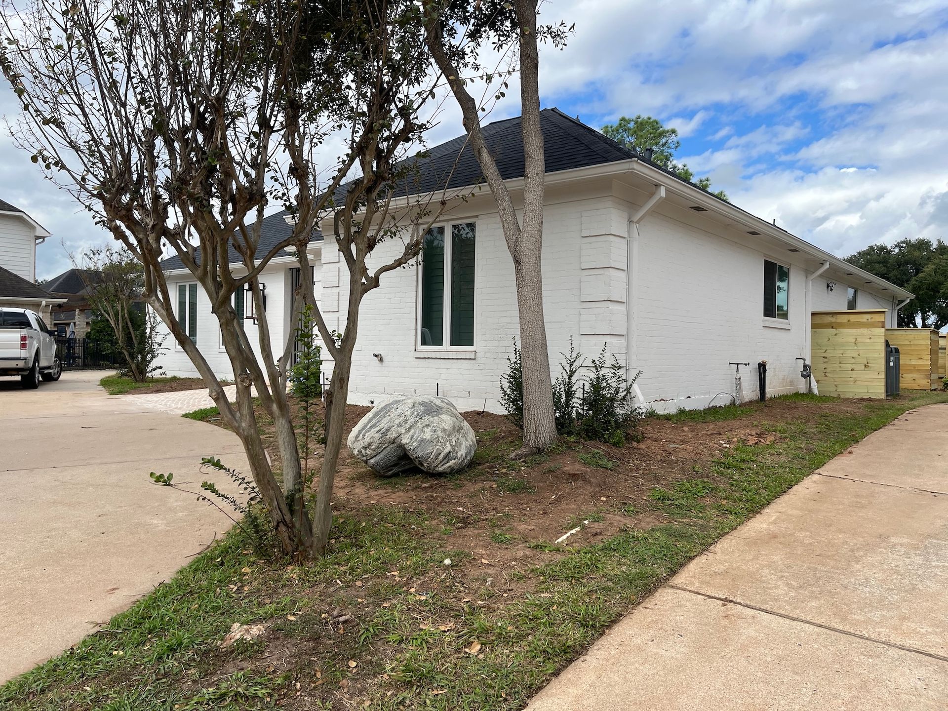 White-painted brick house with a black roof, flanked by trees and a driveway on a cloudy day.