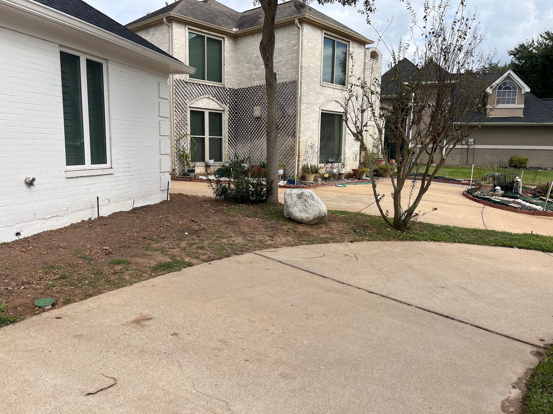 Driveway leading to a two-story home with a white exterior and a rock in the front yard.