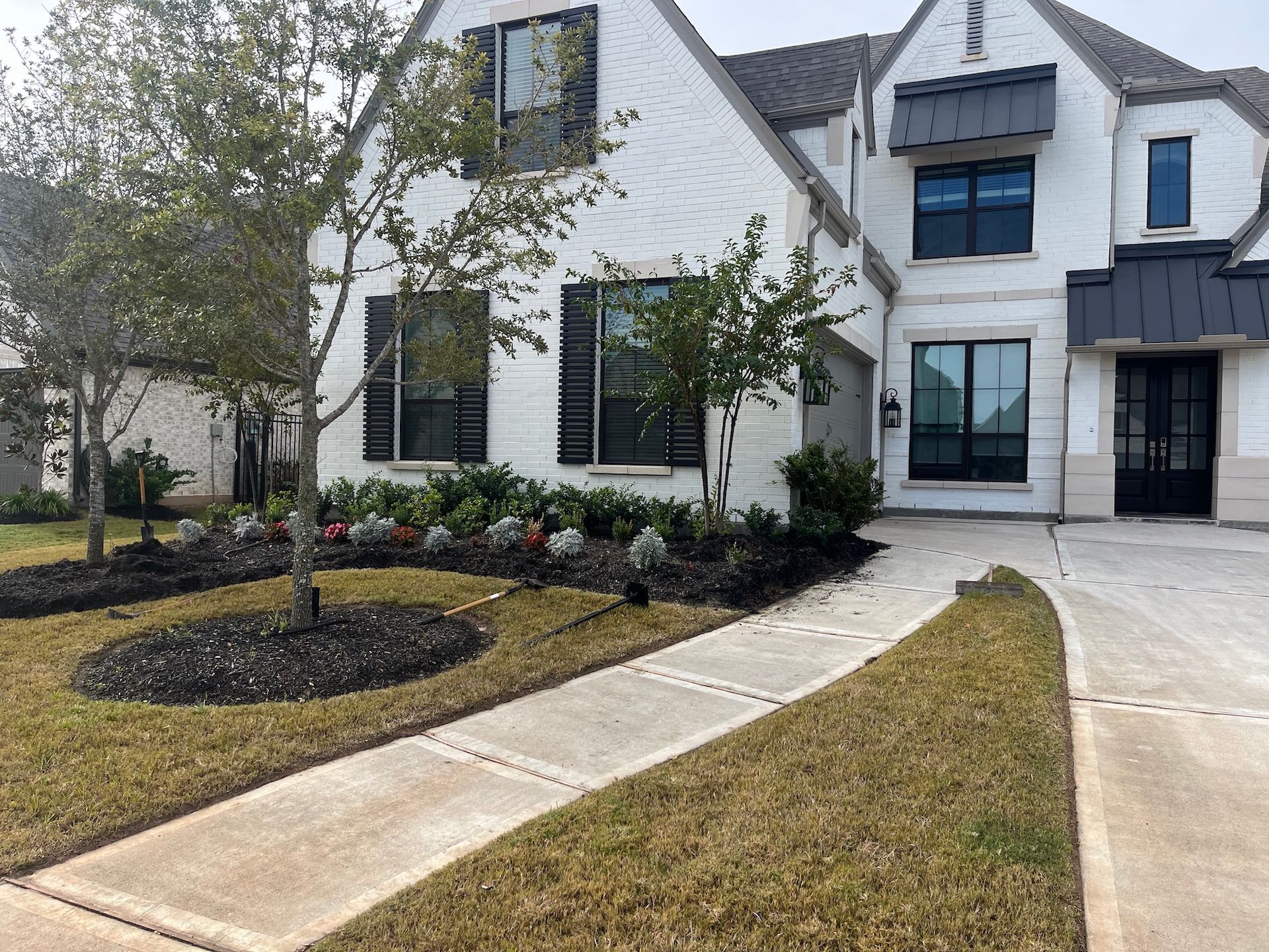 White house with black trim and a landscaped front yard. A concrete walkway leads to the front door.