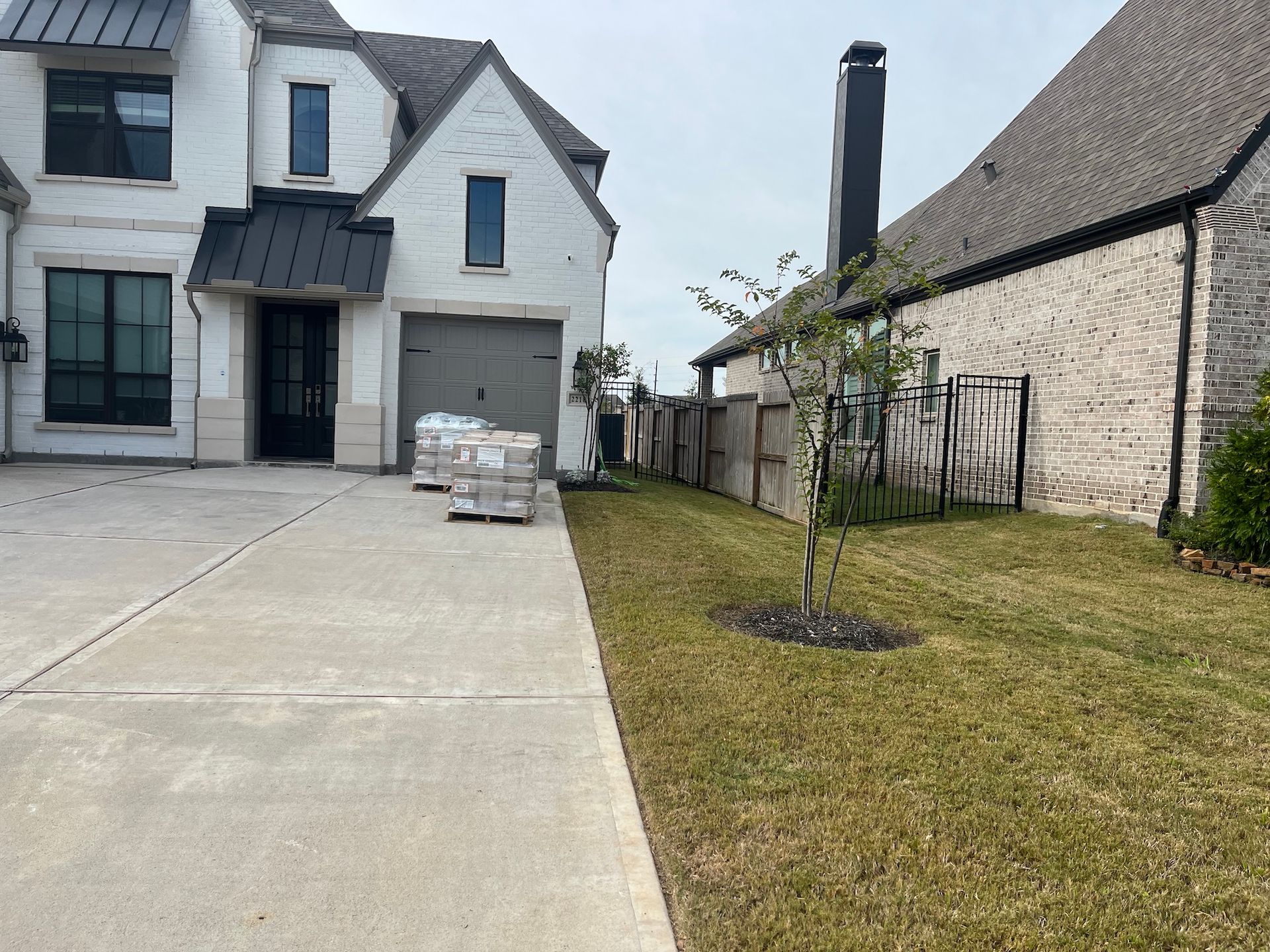 Exterior view of a house with a concrete driveway, grass, and a brick fence under a cloudy sky.