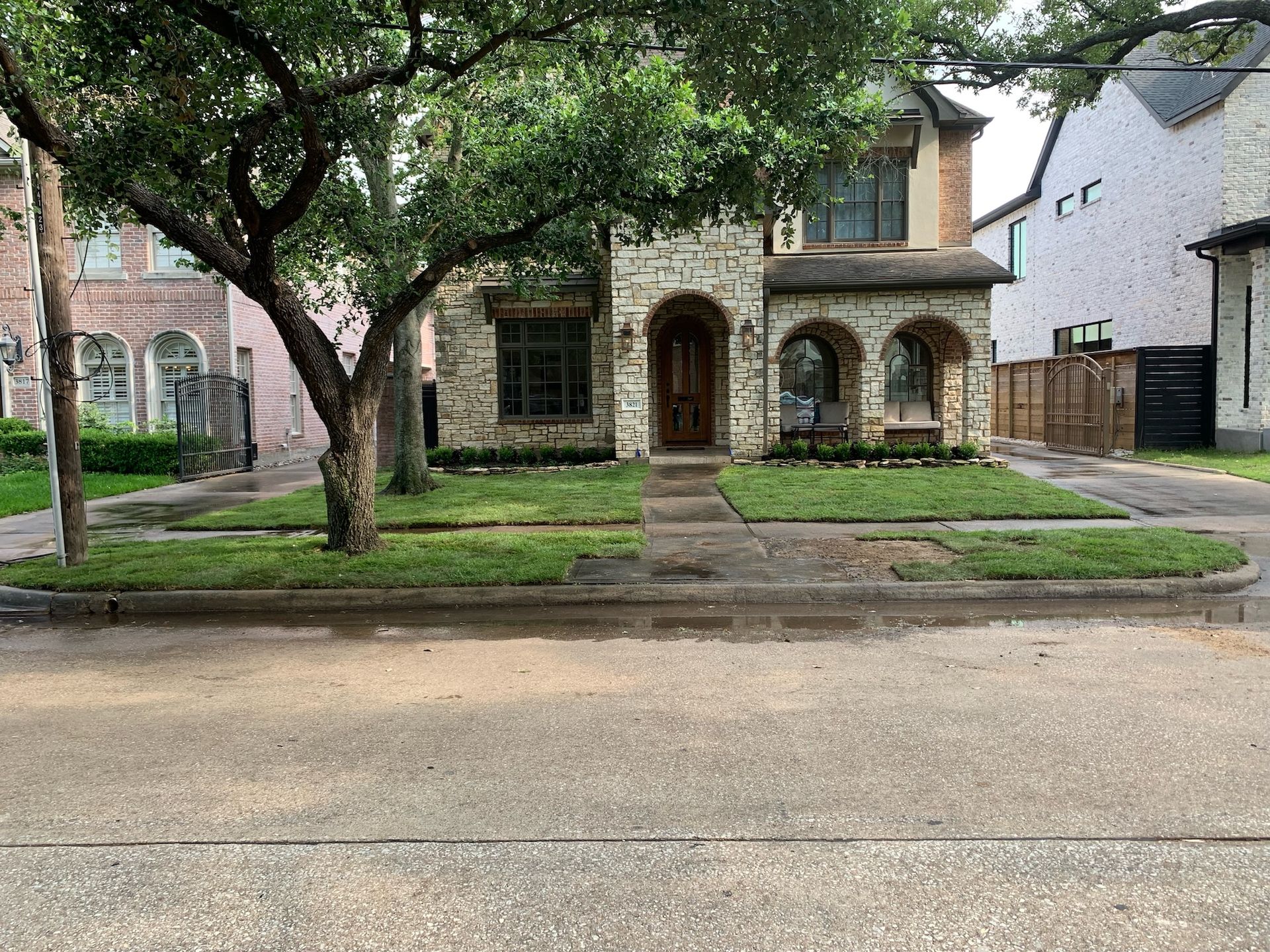 House with brick facade, arched entryway, and mature tree in front yard, on a street.