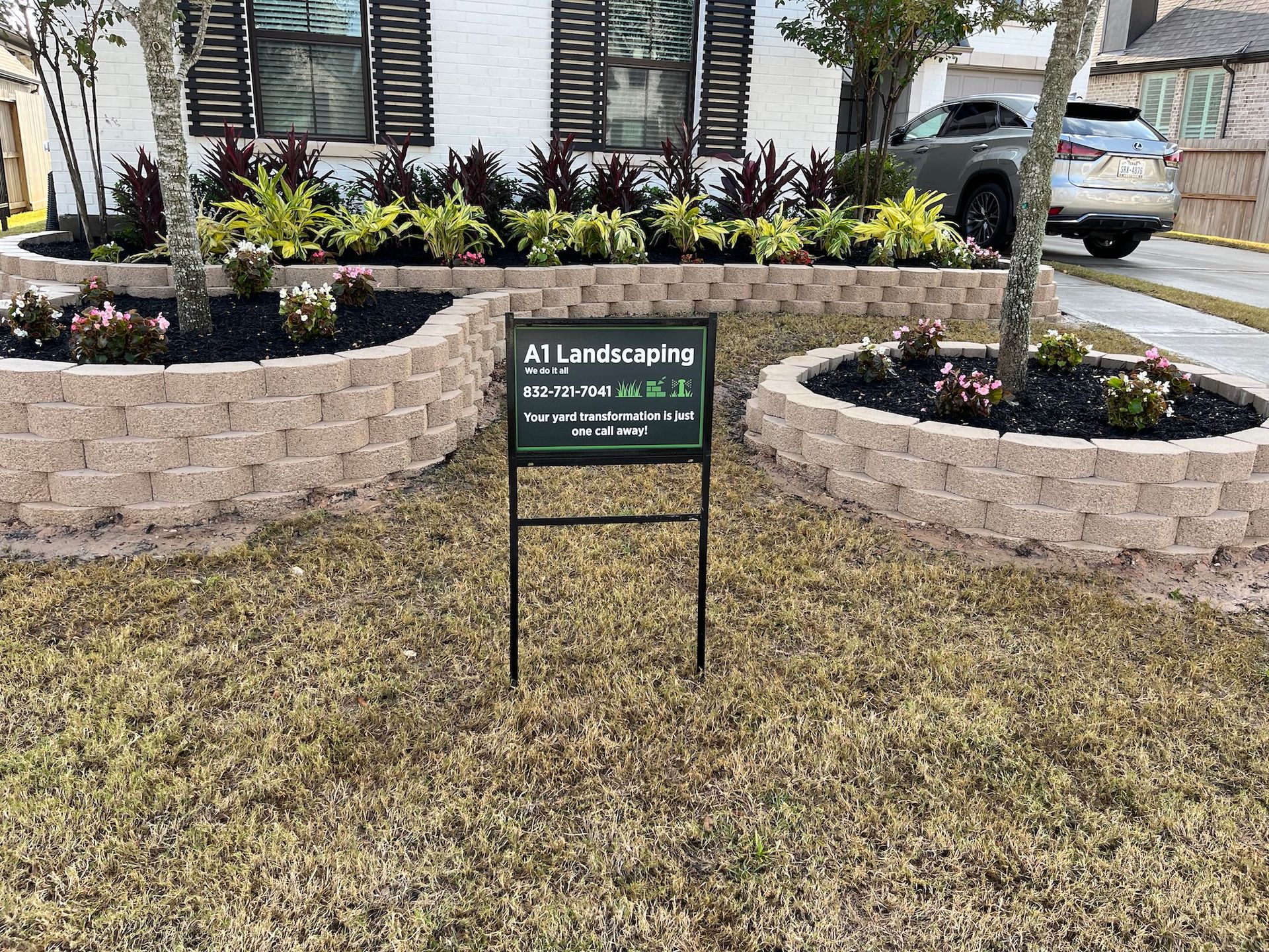 Landscaped yard with retaining walls, flowerbeds, and a sign that reads 