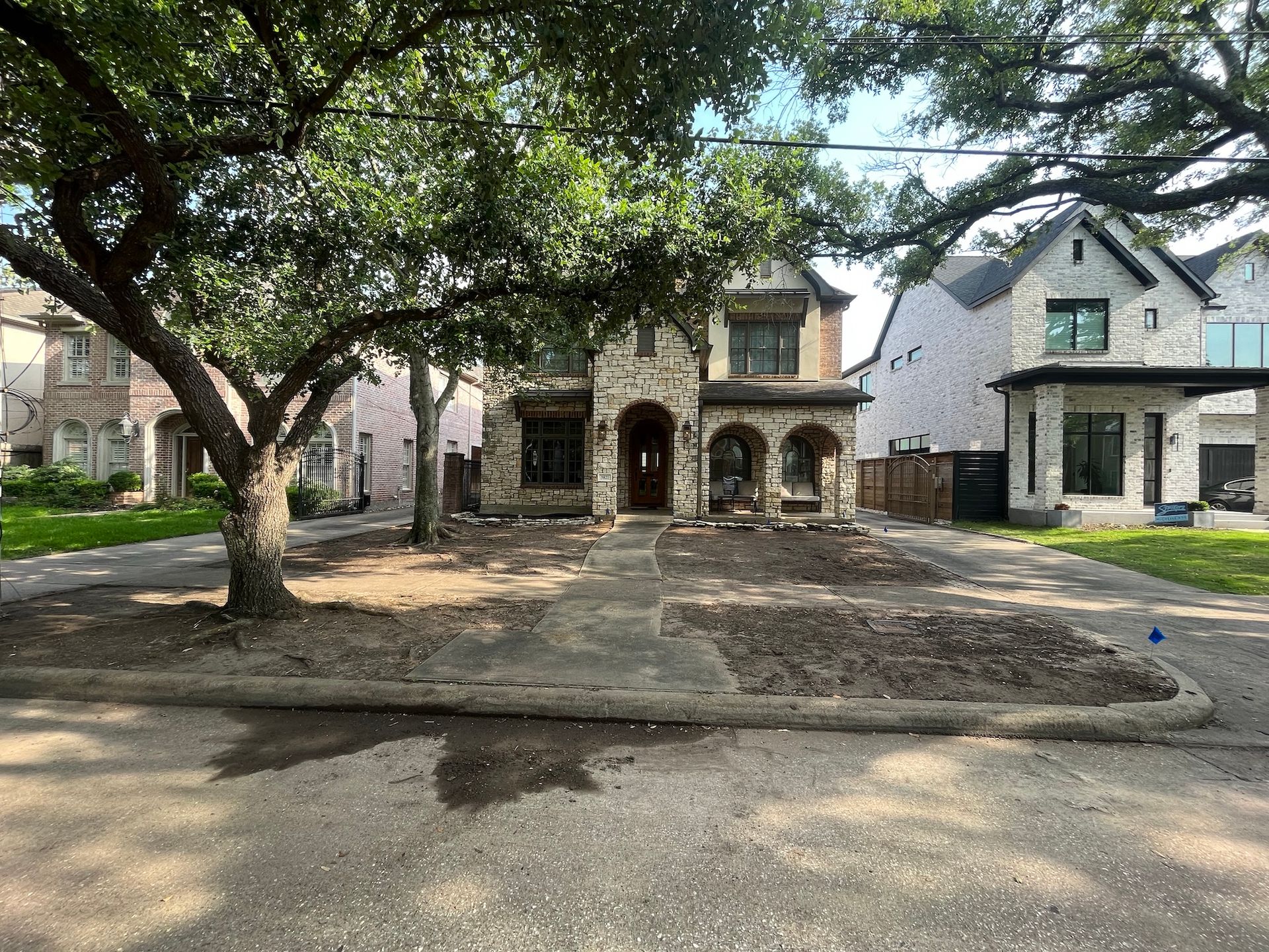 A two-story brick home with arched entryway and bare landscaping. Street view, sunny day.