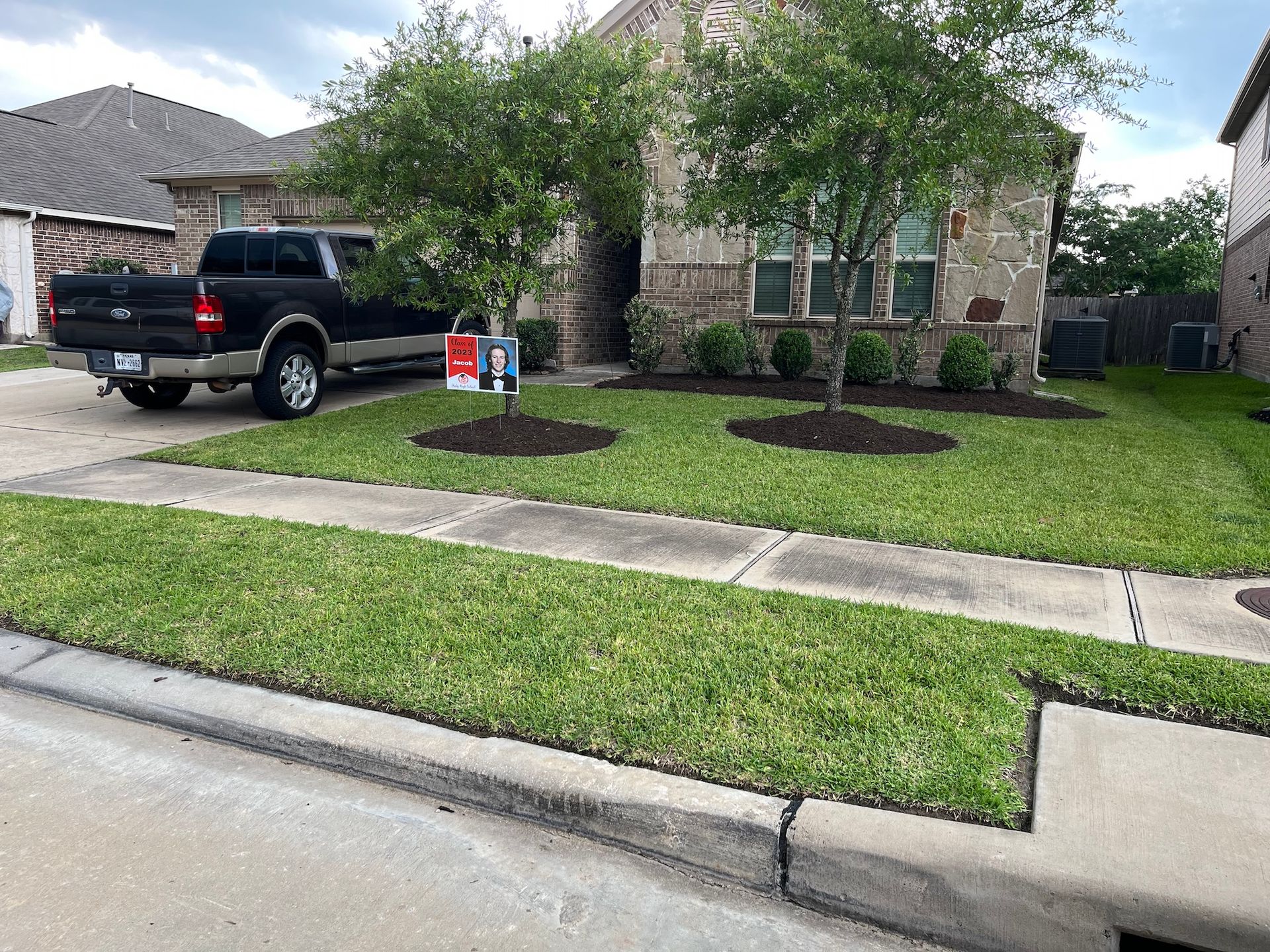 Well-manicured lawn and a home with stone facade. A black truck is parked in the driveway. Trees with mulch.