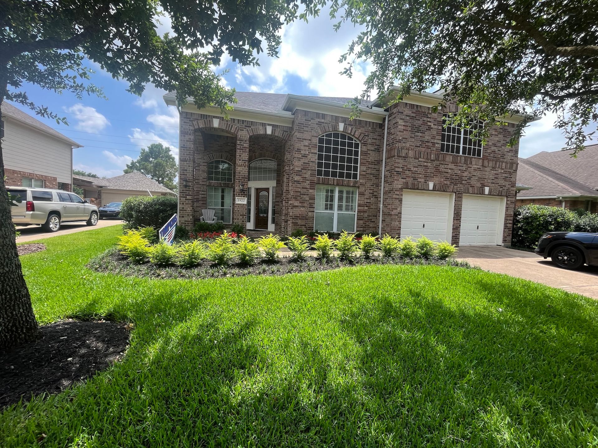 Two-story brick house with a green lawn and manicured flower beds.  Two-car garage on the right.
