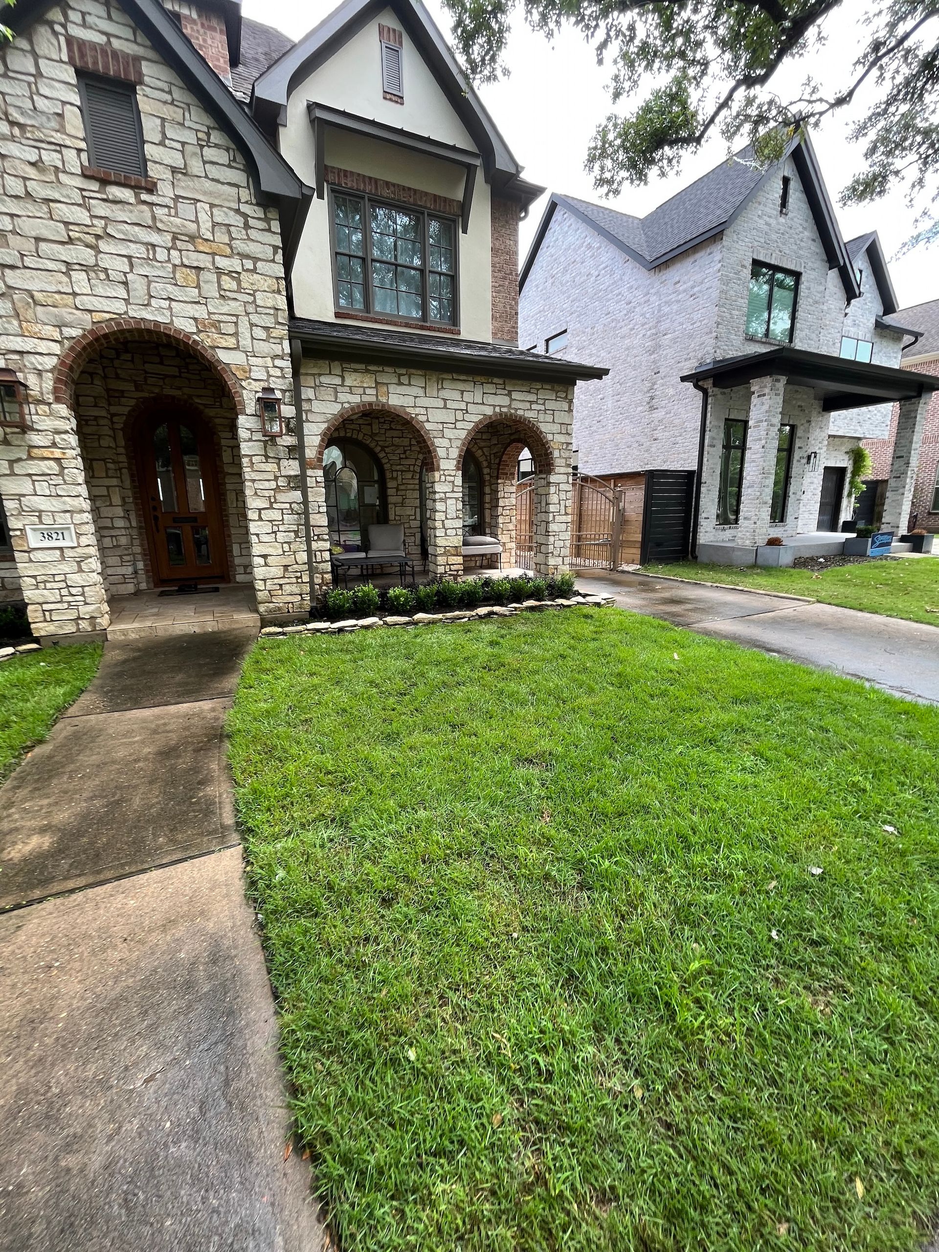 Stone houses with green lawns and a sidewalk on a sunny day.