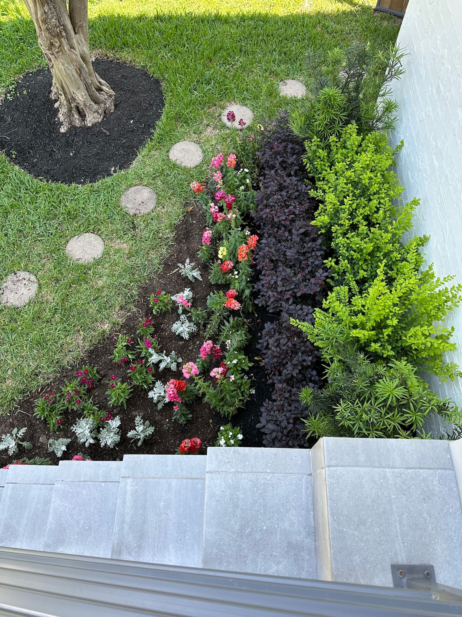 Garden bed with flowers and shrubs next to a gray stone staircase and green lawn.