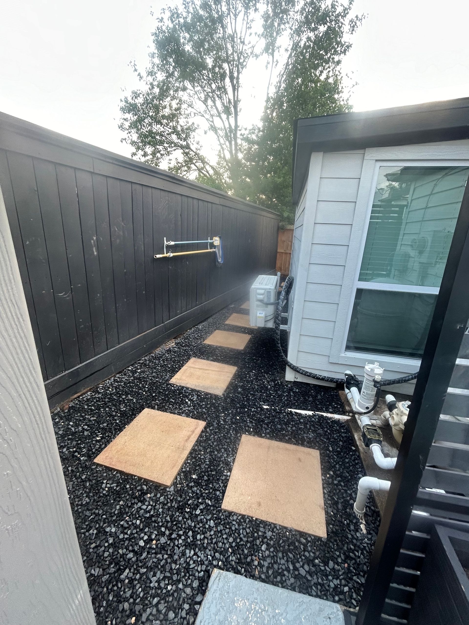Pathway with stepping stones, black gravel, and black fence beside a white building and trees.