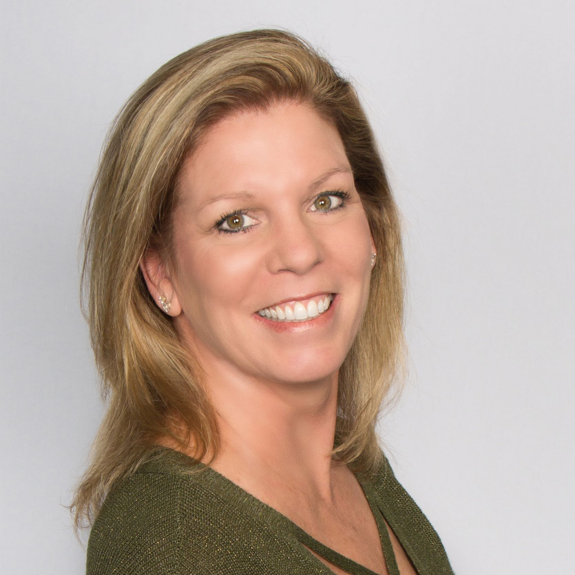 Woman smiling, wearing a green top. Shoulder-length blonde hair. Neutral background.