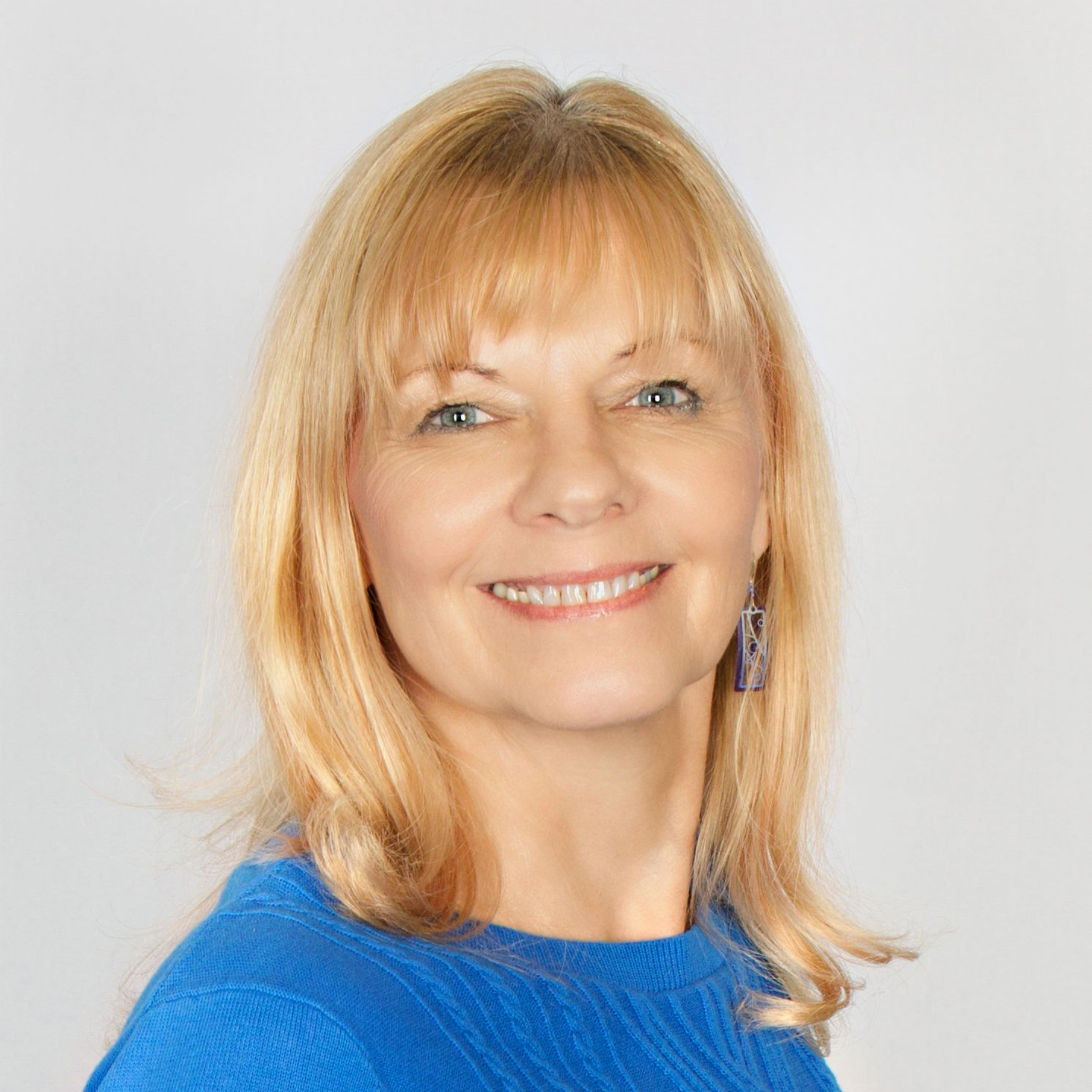 Woman with blonde hair wearing a blue sweater smiles, against a gray background.