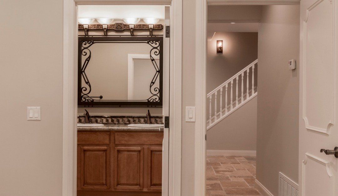 Bathroom doorway looking into vanity, hallway with stairs, beige walls, brown cabinets.