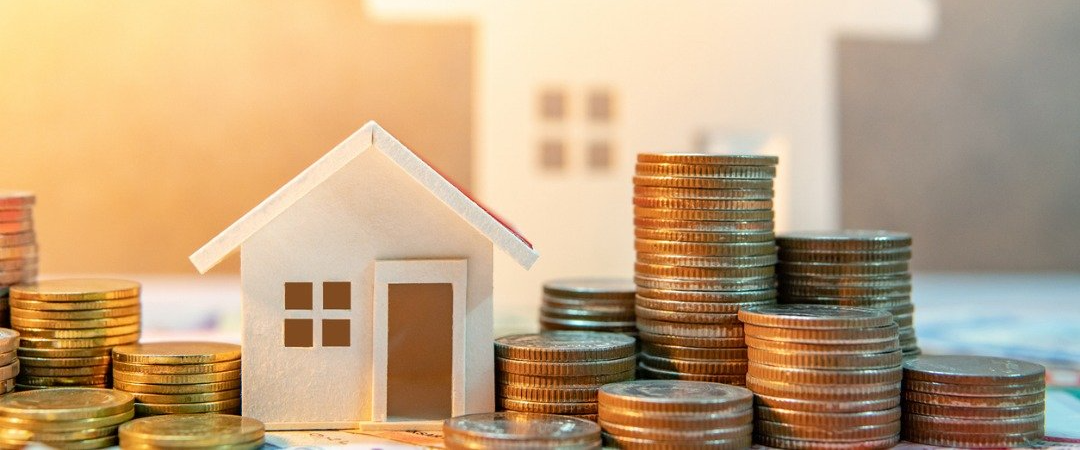 A small model house and stacks of coins, suggesting real estate investment.