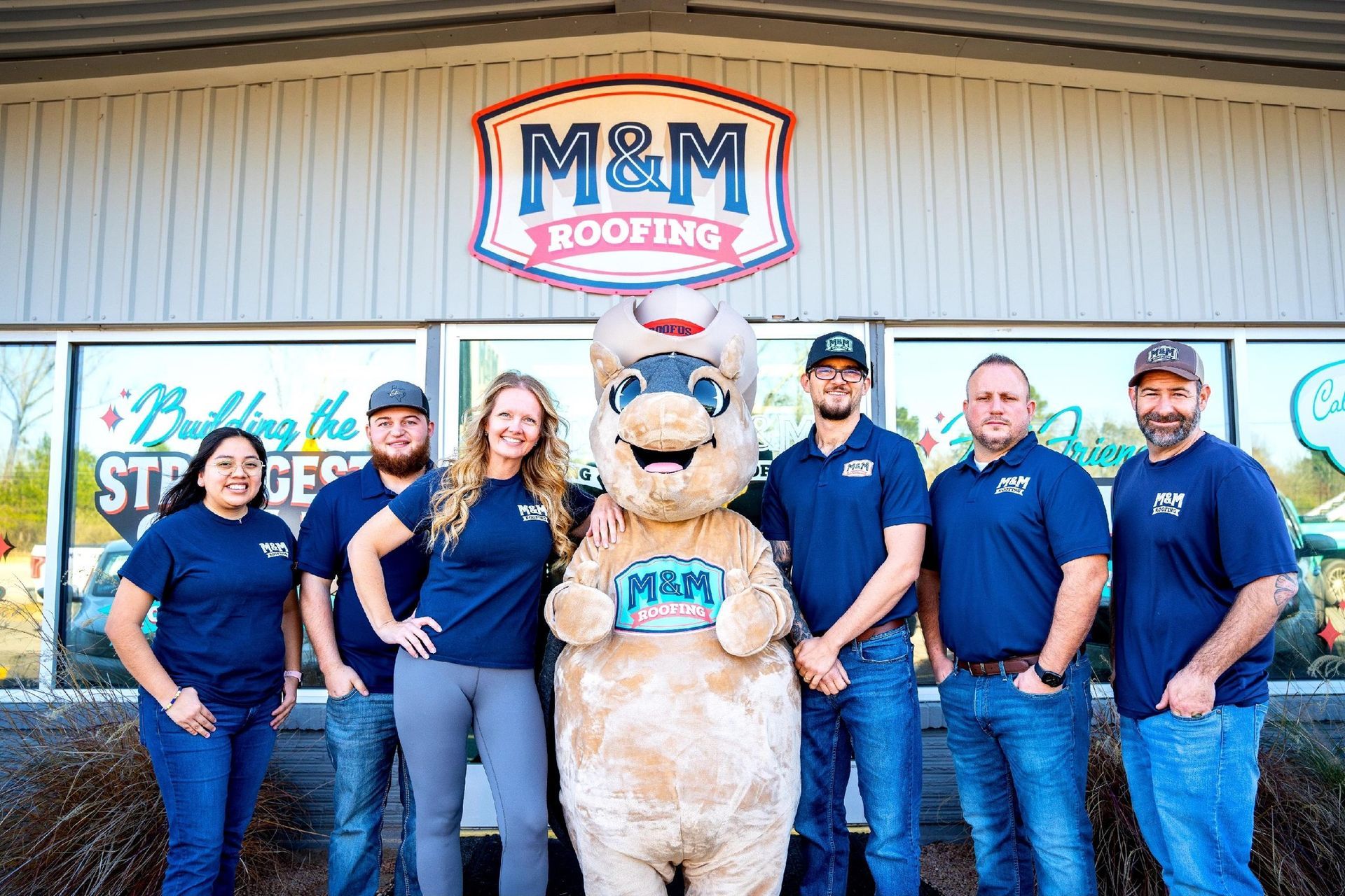 Roofing company team posing outside office with mascot bear in blue shirts