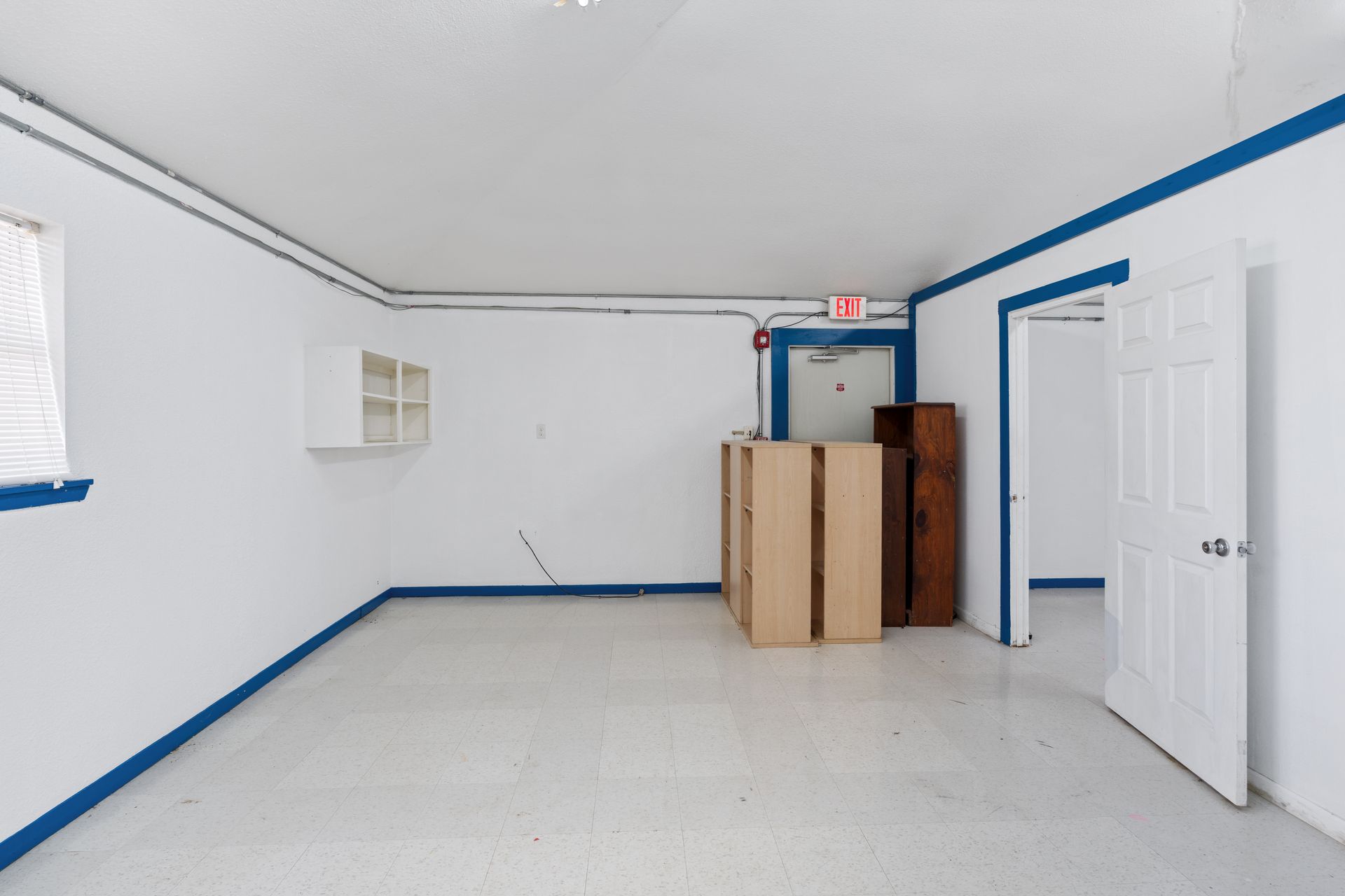 Empty white room with blue trim, a wall shelf, and stacked cardboard boxes near an open door.