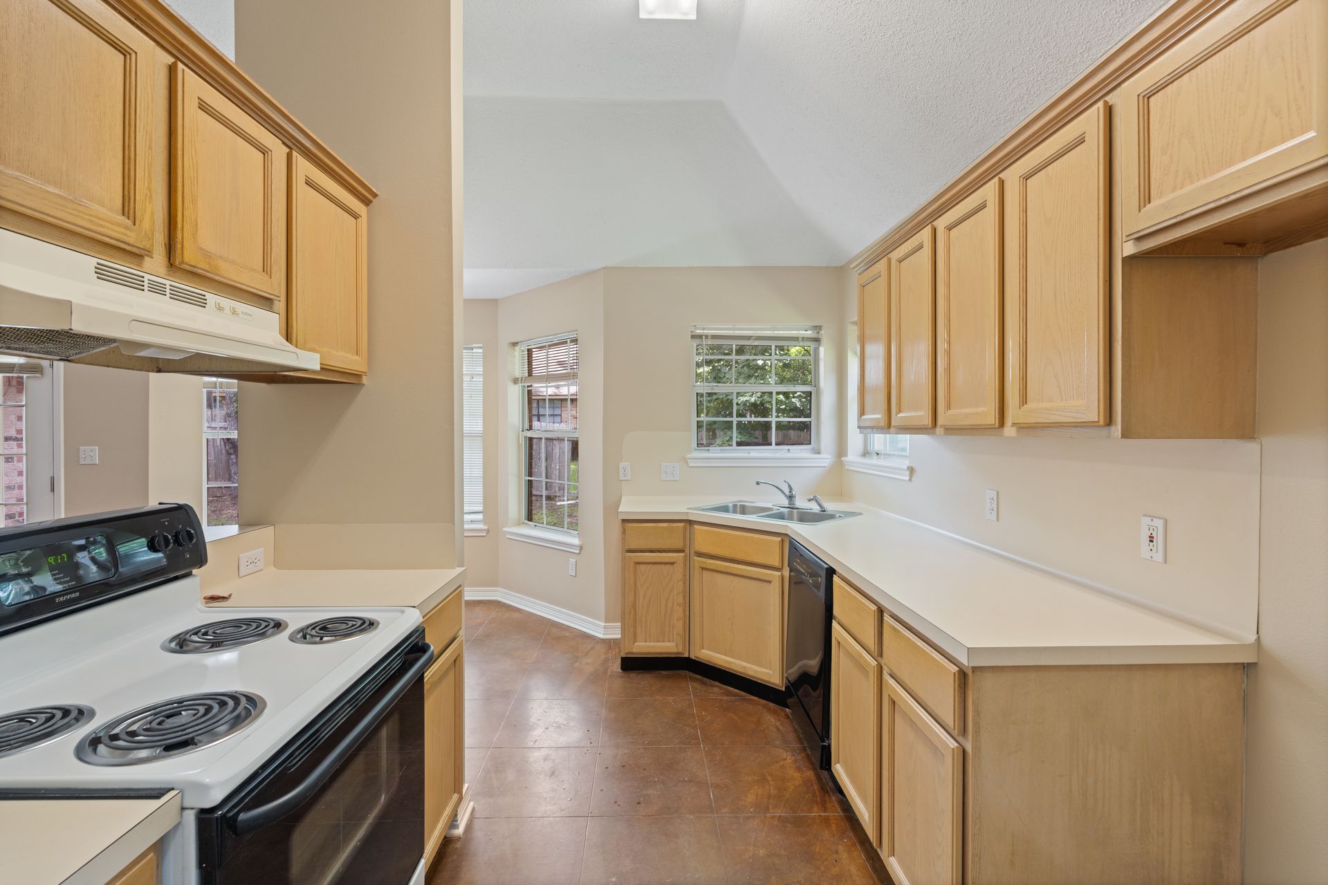 Bright kitchen with wood cabinets, white countertops, and a white stove near a windowed dining nook.