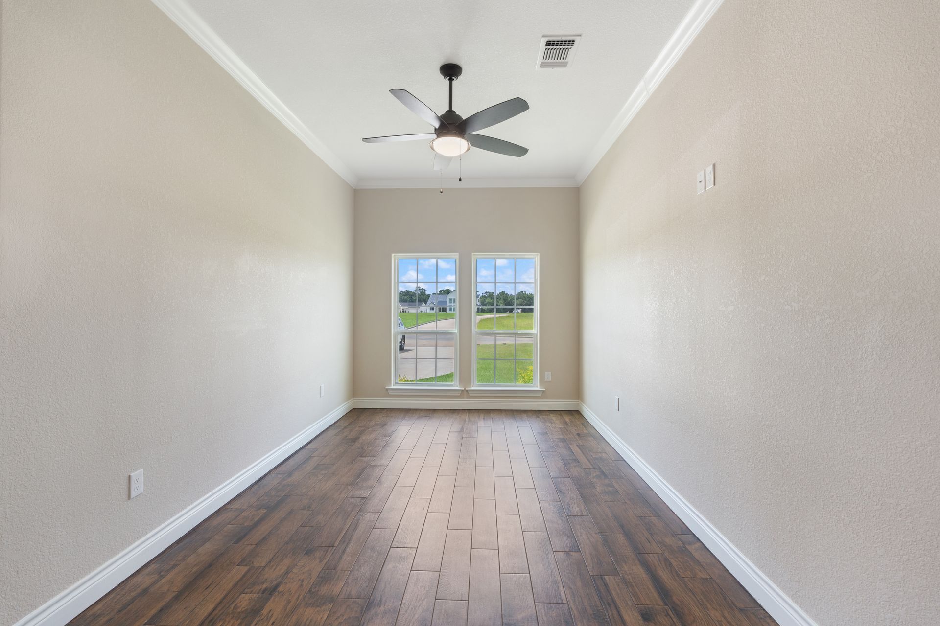 Empty narrow room with wood floors, white walls, ceiling fan, and double doors opening to a grassy view.