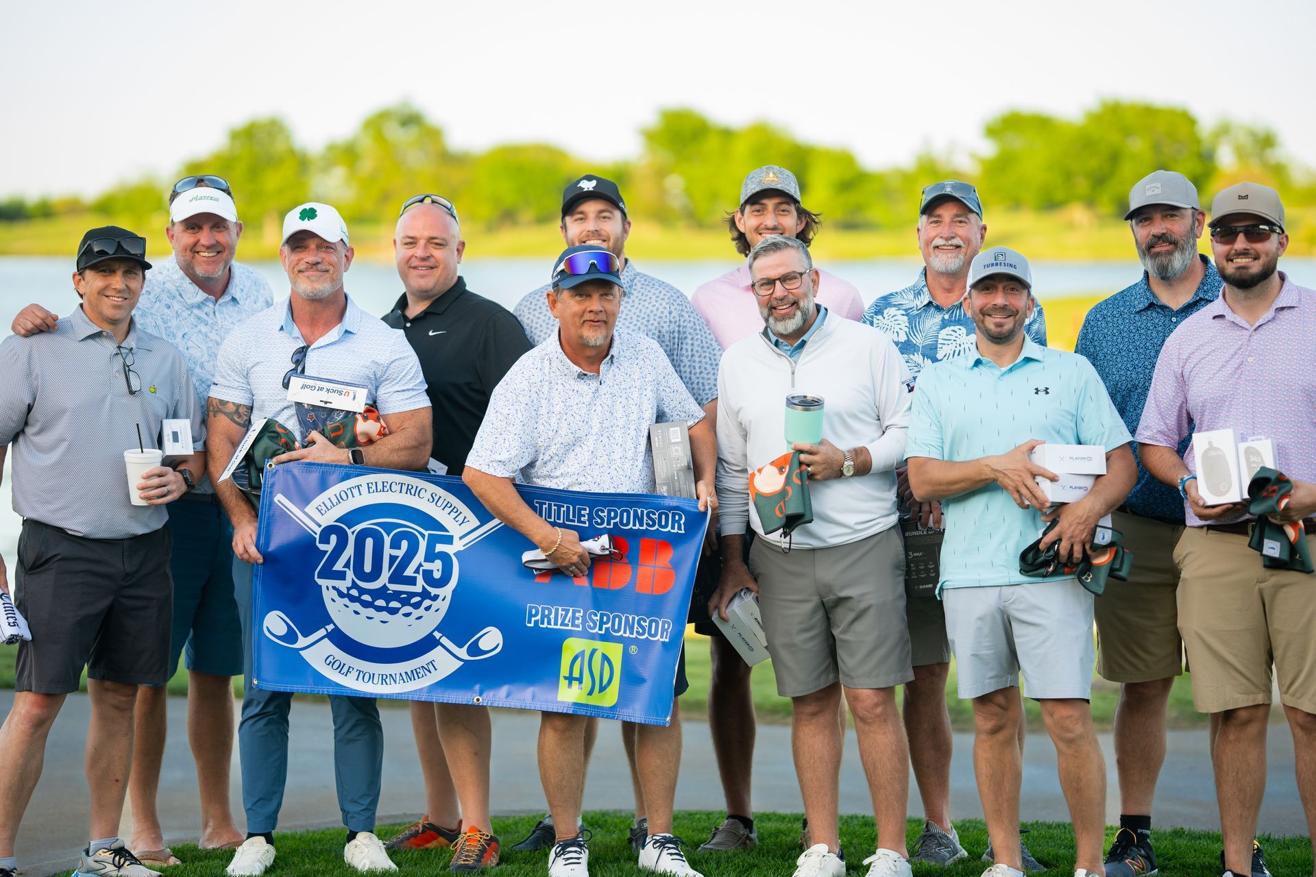 Group of golfers posing with a blue 2025 banner on a golf course, holding drinks and smiling