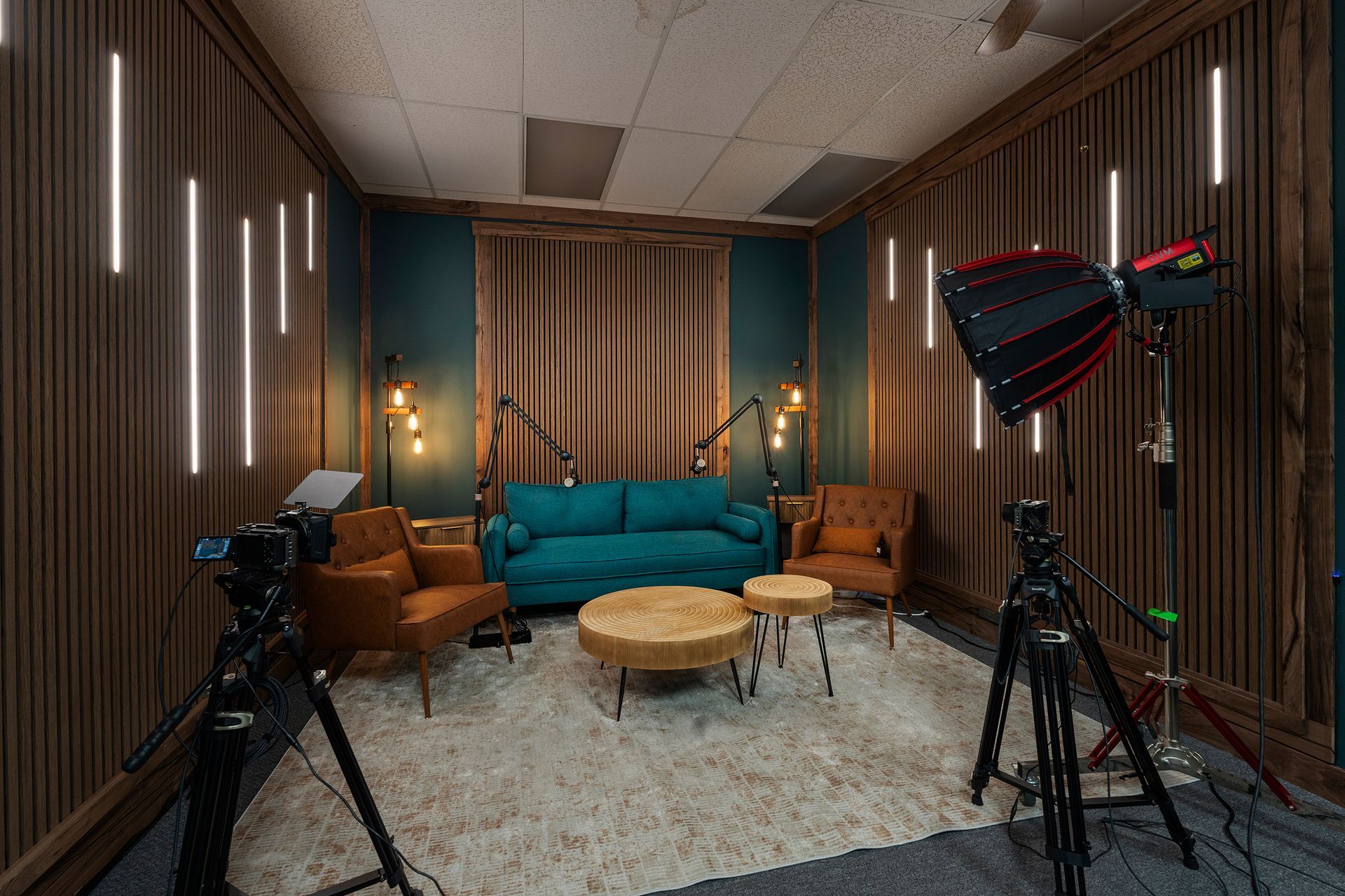 Podcast studio with teal couch, armchairs, rugs, and camera and lights on tripods