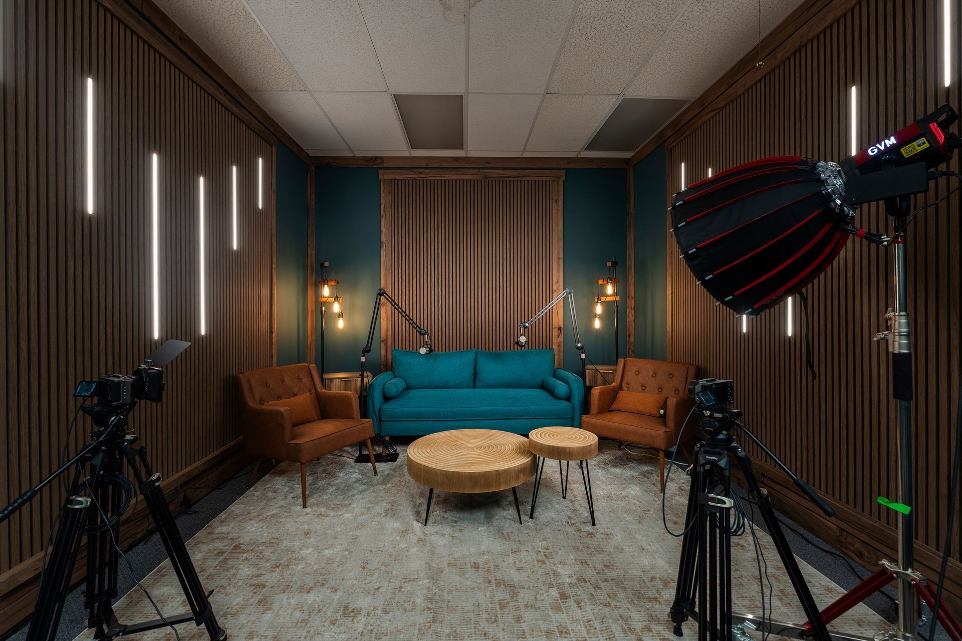 Podcast studio with teal sofa, brown chairs, microphones, and cameras in a soundproof room