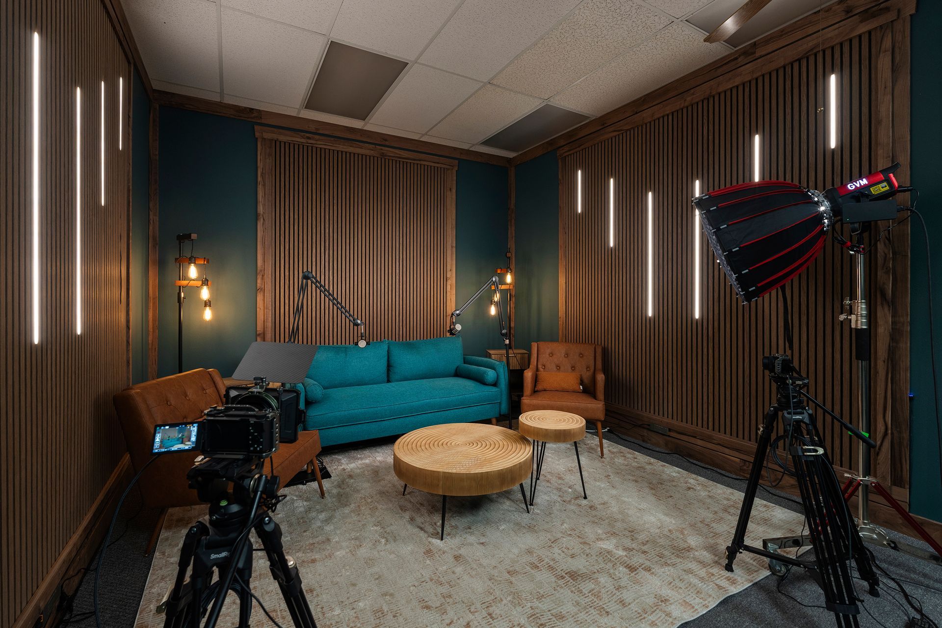 Studio recording setup with teal couch, microphones, cameras, and softbox lights in a sound-treated room