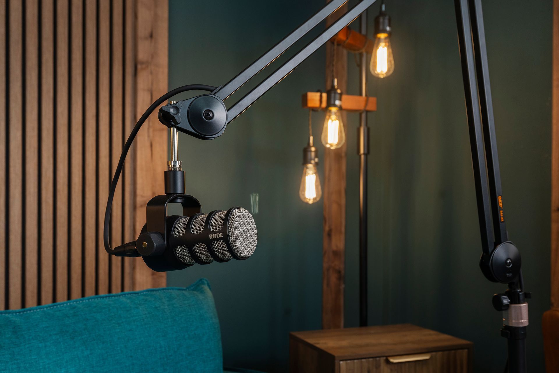 Podcast microphone on boom arms in a cozy studio with hanging Edison bulbs and a teal chair
