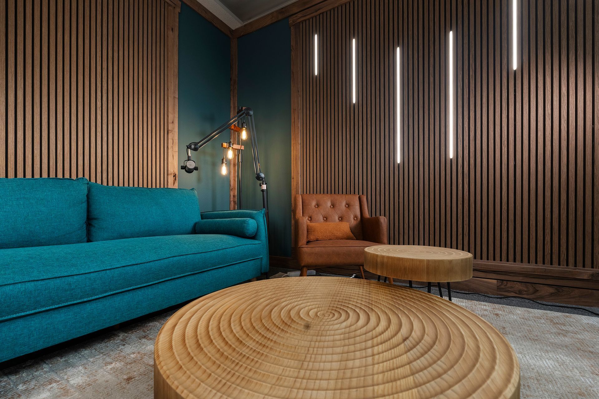 Modern lounge with teal sofa, tan chair, round wooden table, and wood slat walls