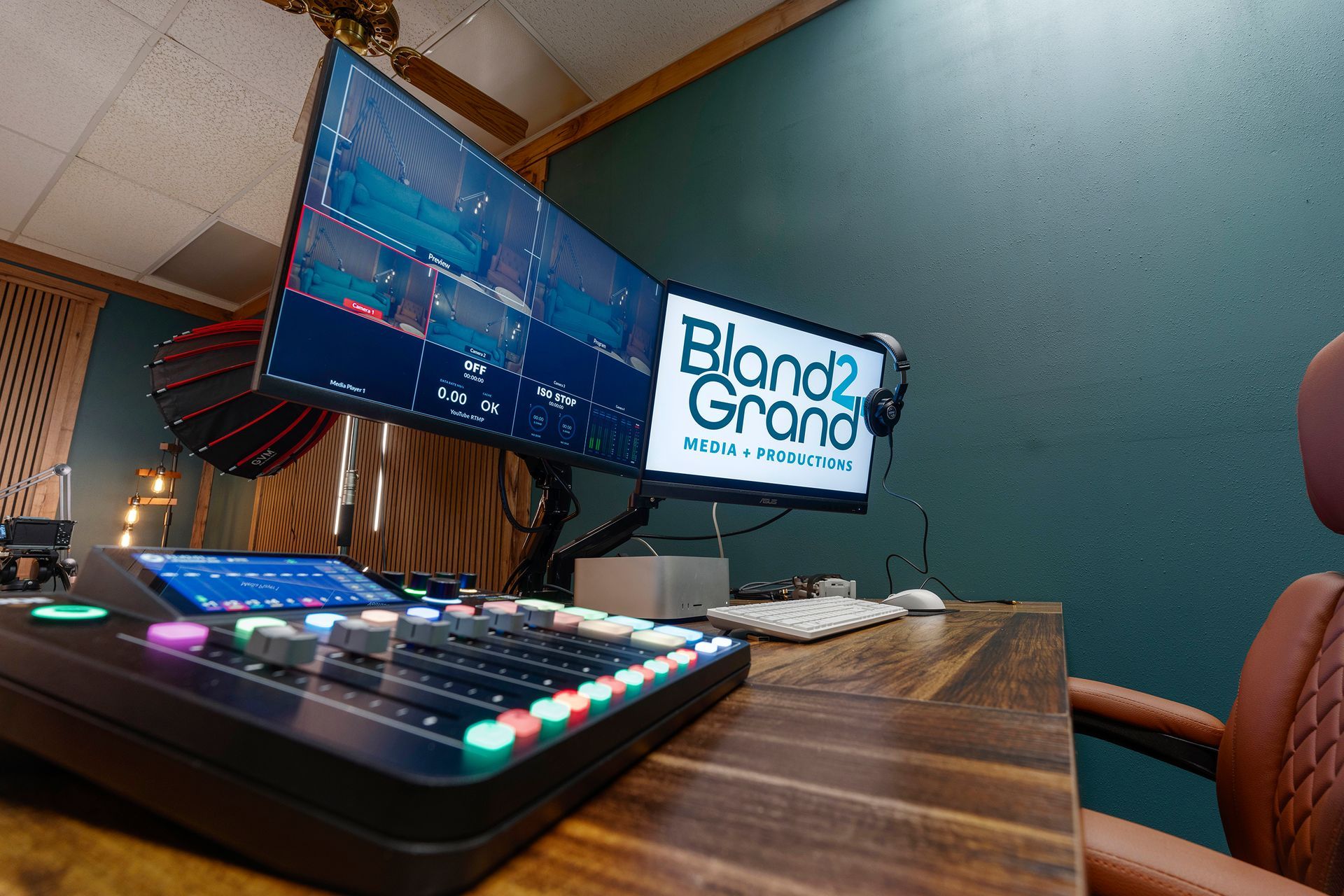 Podcast studio desk with colorful audio mixer, dual monitors, and a teal wall backdrop