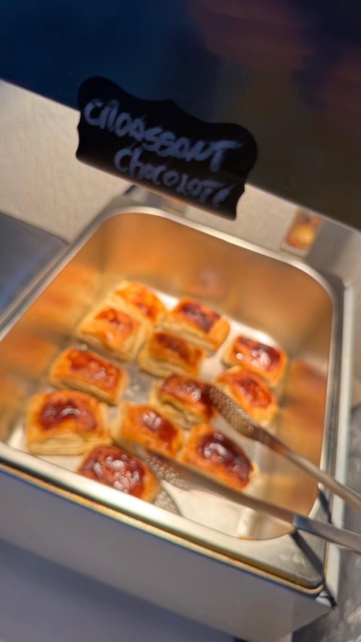 Bandeja de croissants glaceados com pinças em uma vitrine de padaria com a etiqueta “croissant de chocolate”.