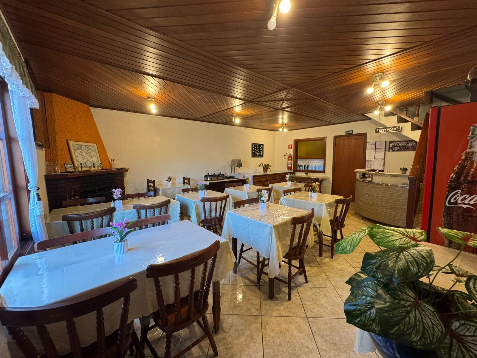 Sala de jantar rústica de restaurante com toalhas de mesa brancas, cadeiras de madeira e teto com painéis de madeira.