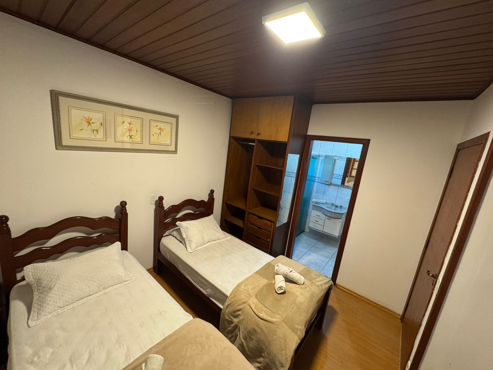 Quarto de hotel pequeno com duas camas de solteiro, móveis de madeira e janela para uma varanda.
