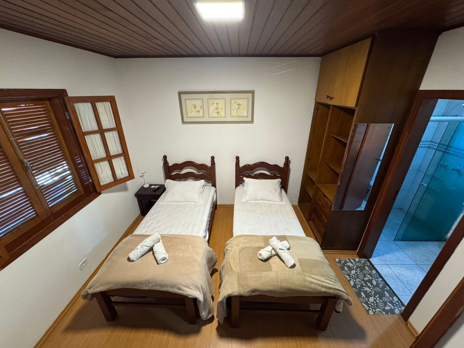Duas camas de solteiro em um pequeno quarto com painéis de madeira, janelas abertas e porta aberta para o banheiro.