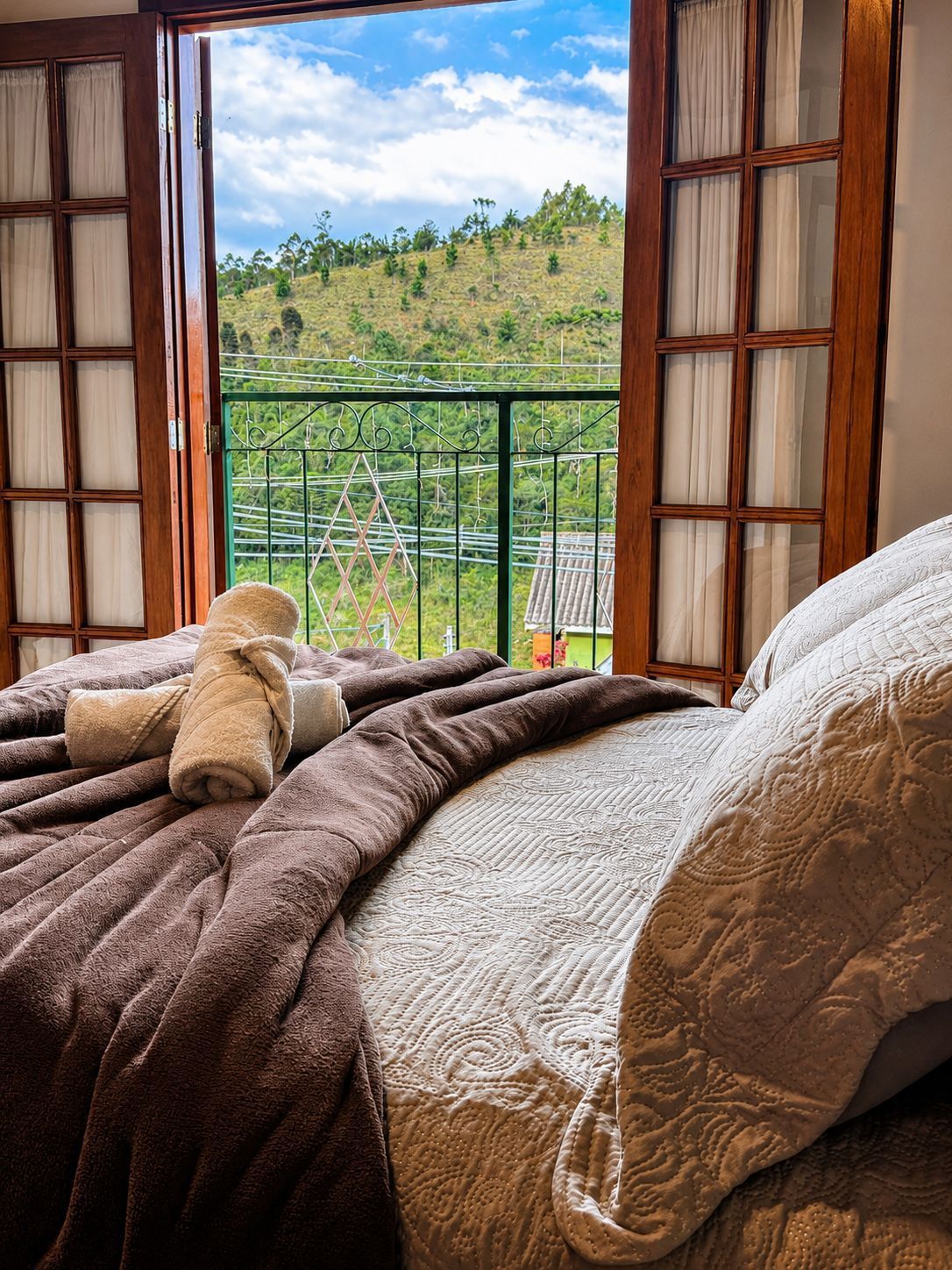 Cama aconchegante junto à janela aberta com vista para a montanha e a floresta, com vista para uma encosta verdejante.