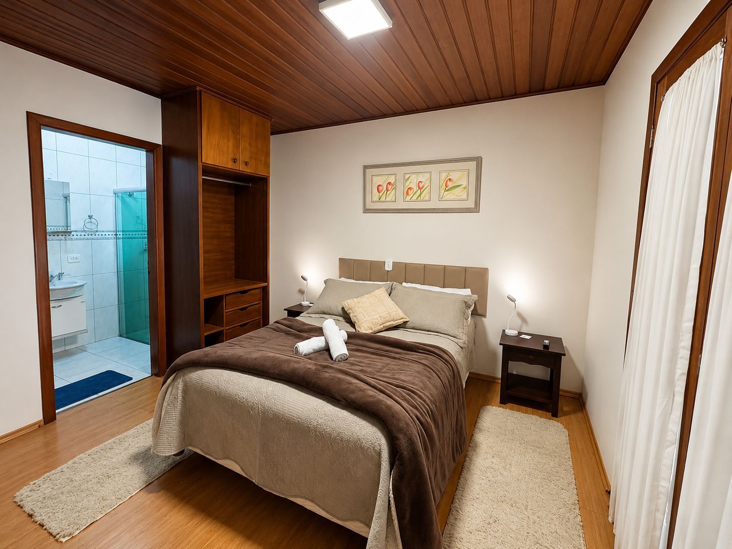 Quarto com cama arrumada, teto de madeira e porta do banheiro aberta à esquerda.