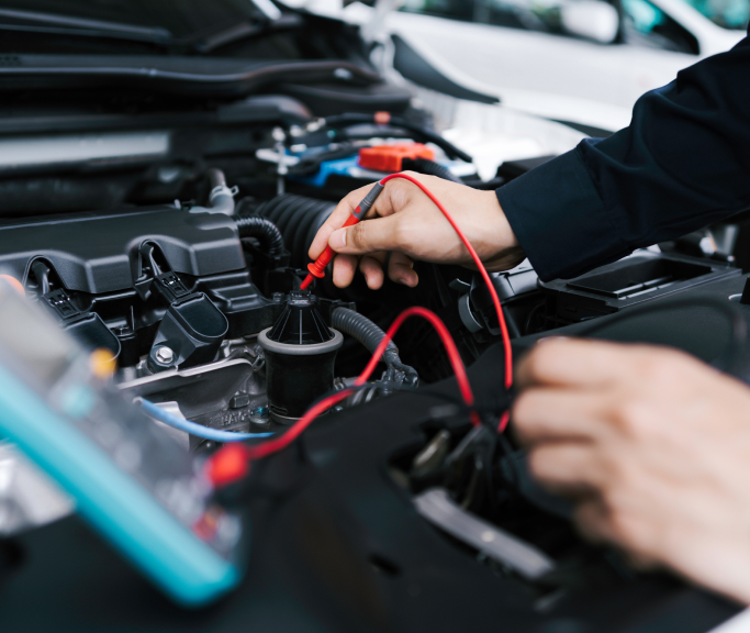 A person is working on a car engine with a multimeter. | Greatway Tire and Auto Center