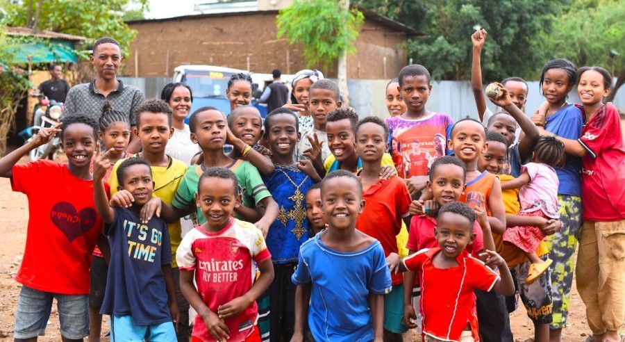 Group of children posing outdoors in colorful clothes, smiling and cheering with raised arms.