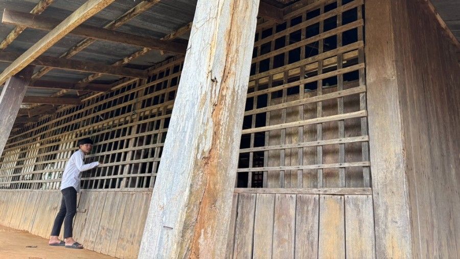 Person standing at a wooden building, looking through barred windows on a covered porch.