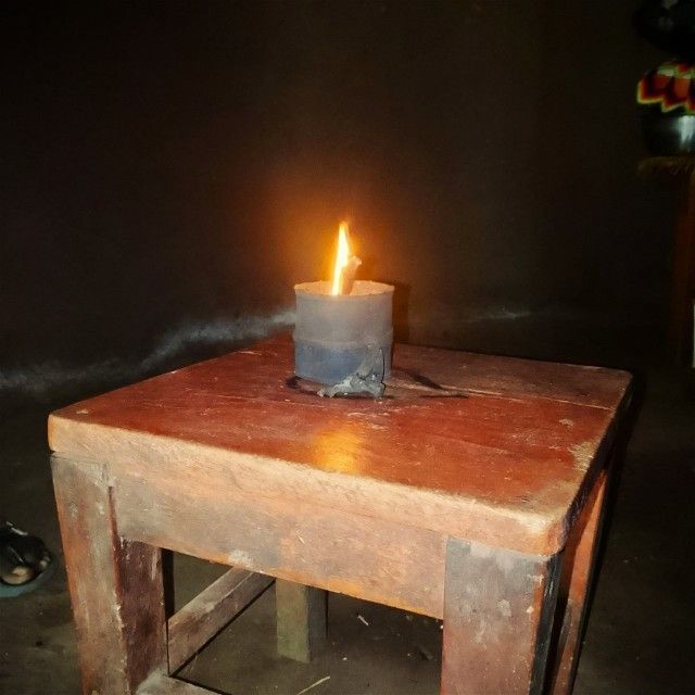 A lit candle in a black holder on a worn wooden table in a dark room