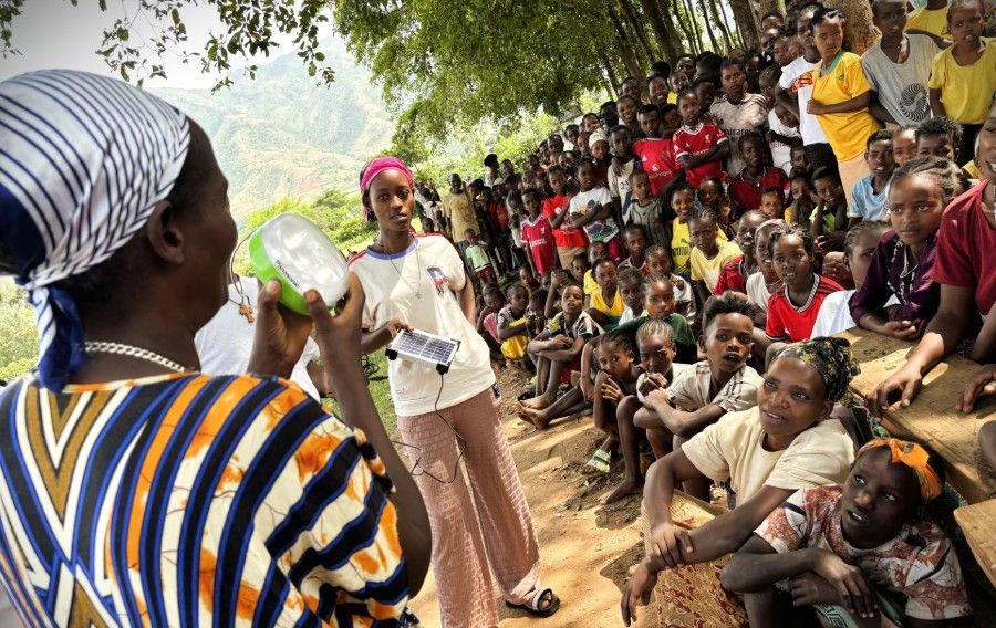 Woman speaking into a megaphone to a seated crowd outdoors under trees