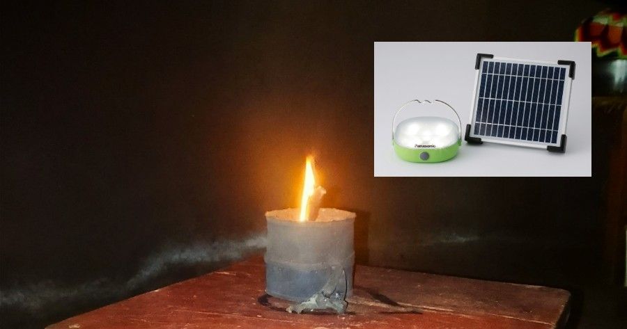 Lit candle on a table beside a small solar panel powering a glass bowl in a dark room