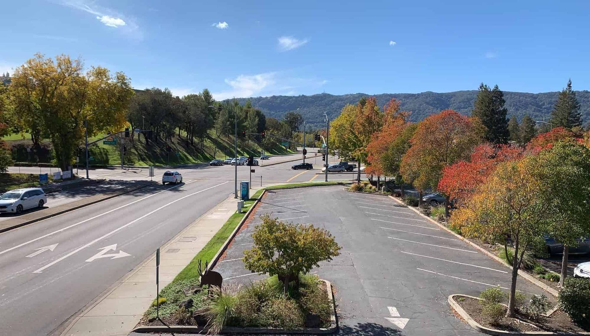 A parking lot and road bordered by colorful autumn trees under a bright blue sky with hills in the distance.