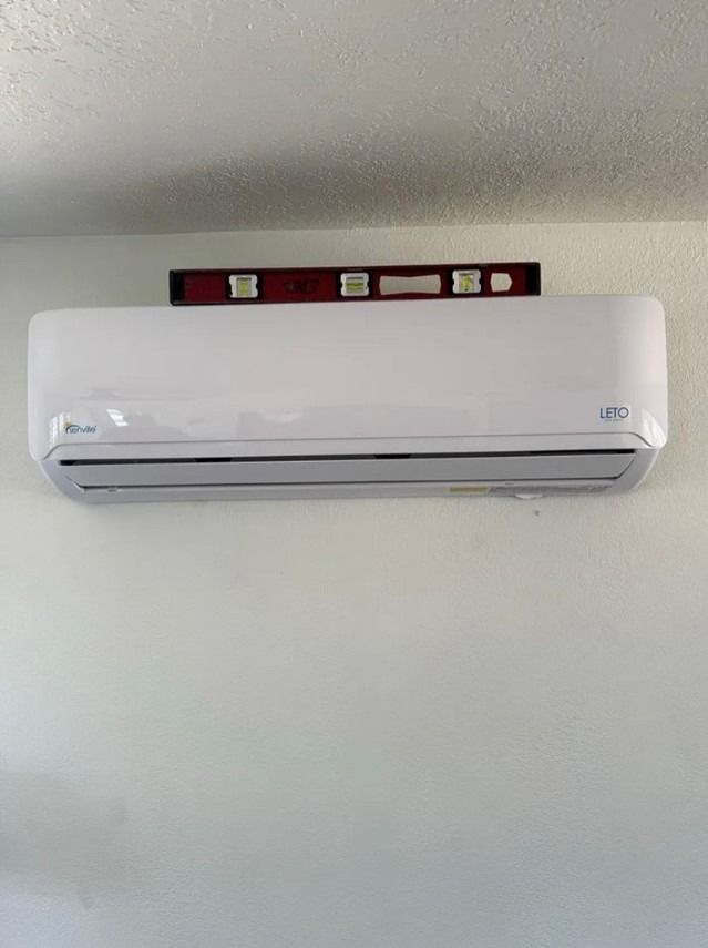 White wall-mounted air conditioner beneath a red level on a light gray wall.