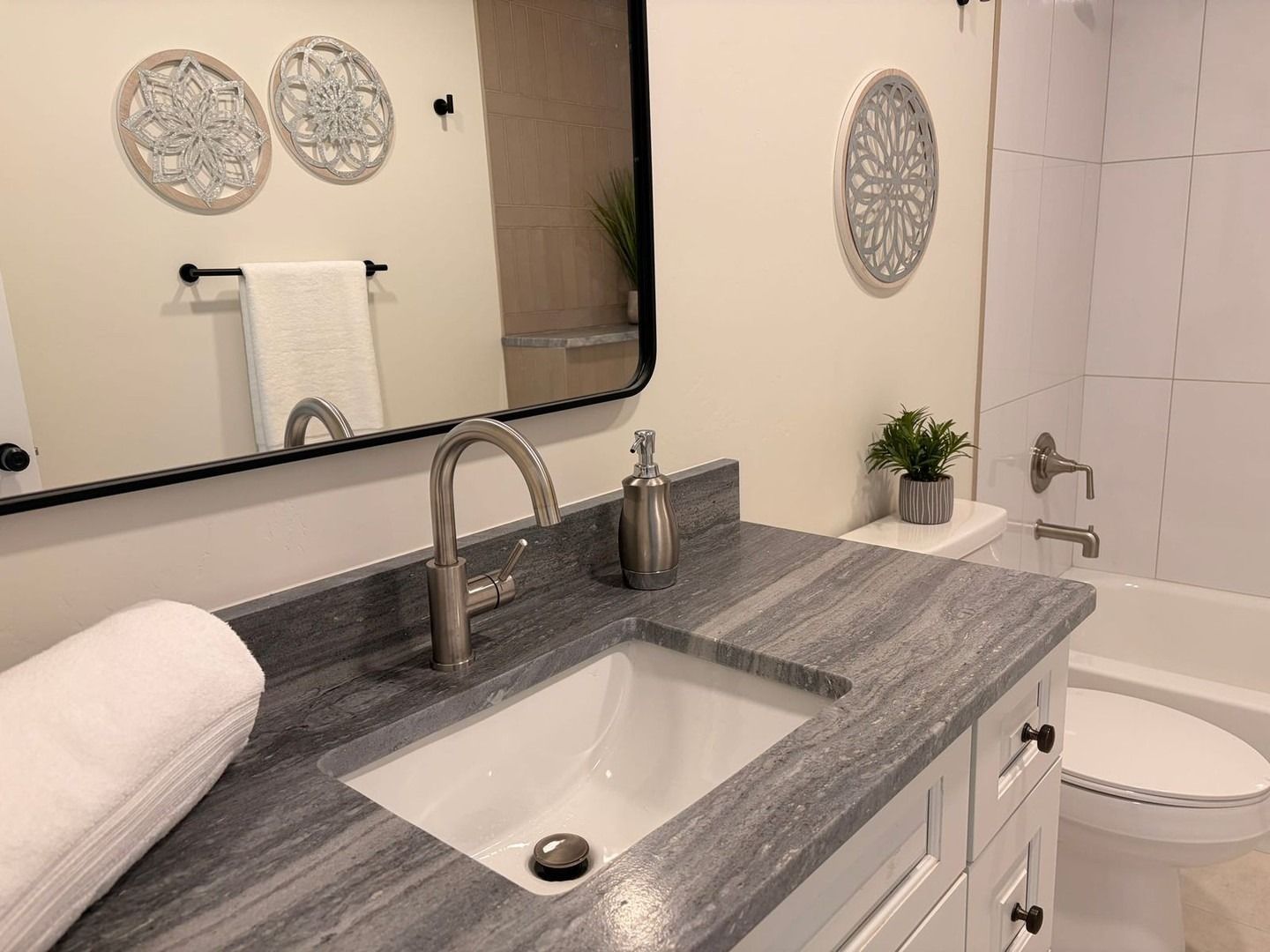 Modern bathroom vanity with marble countertop, sink, mirror, towels, plant, and adjacent bathtub and toilet