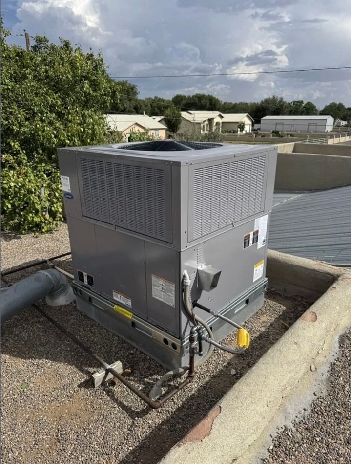 Gray rooftop HVAC unit beside a gravel roof edge, with ducts and vented panels against cloudy sky