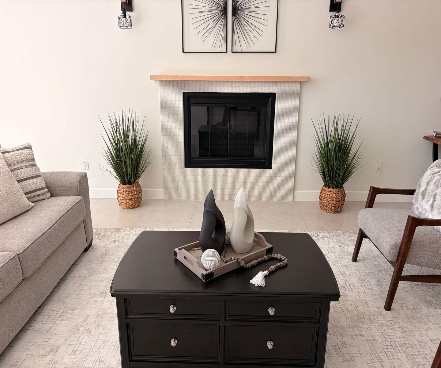 Modern living room with fireplace, beige sofa, coffee table, potted plants, and wall art
